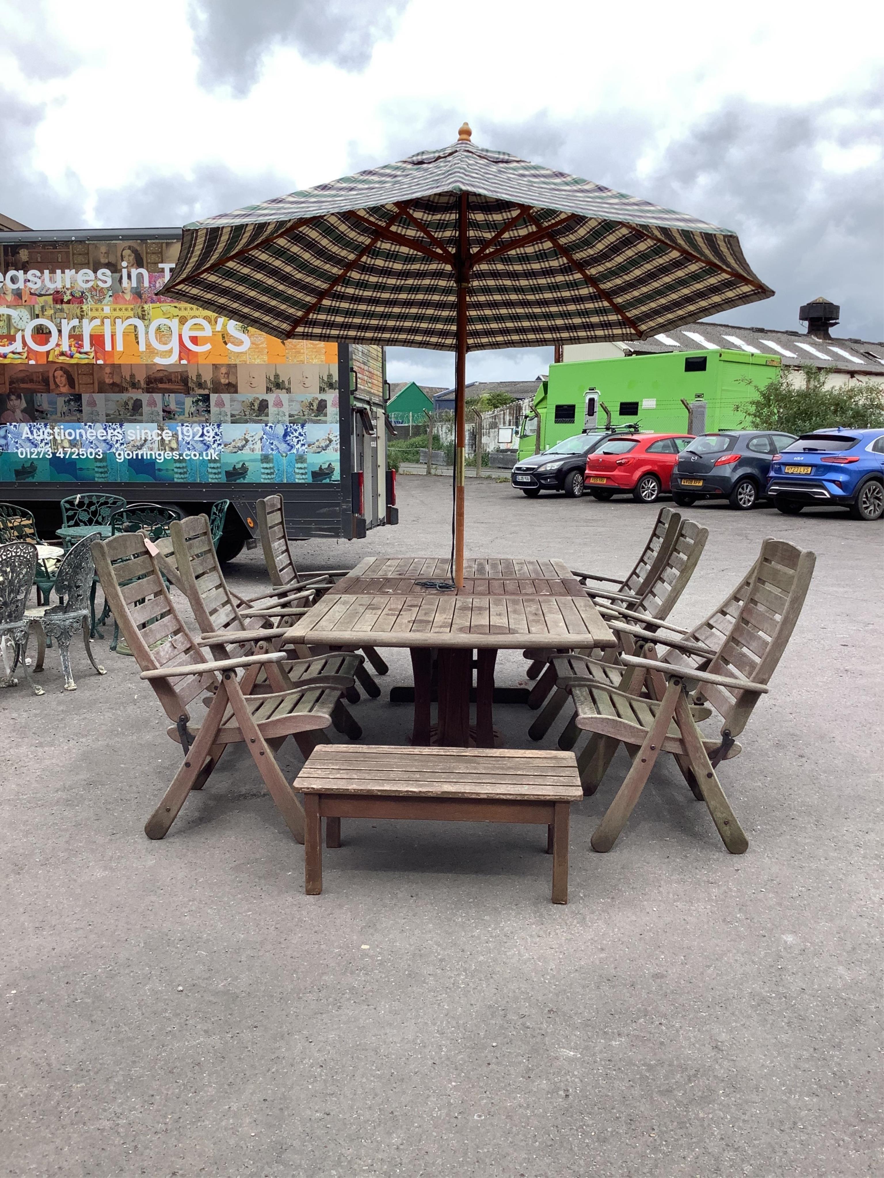 A large rectangular weathered teak extending garden table, width 256cm extended, depth 116cm, height 72cm together with a set of eight teak 'Clarecraft' elbow chairs, two with extending footrests, parasol, cast metal par
